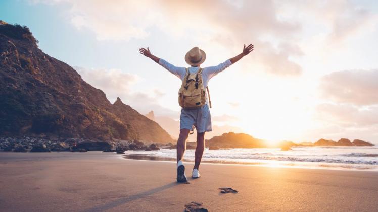 male standing on a sandy beach with arms up in the air